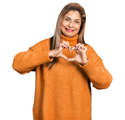 Middle age latin woman wearing turtleneck sweater smiling in love doing heart symbol shape with hands. romantic concept.