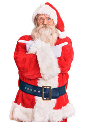 Old senior man with grey hair and long beard wearing traditional santa claus costume pointing to both sides with fingers, different direction disagree