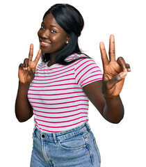 African young woman wearing casual striped t shirt smiling looking to the camera showing fingers...