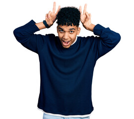 Naklejka premium Young african american man wearing casual clothes posing funny and crazy with fingers on head as bunny ears, smiling cheerful