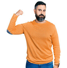 Hispanic man with beard wearing casual winter sweater strong person showing arm muscle, confident and proud of power