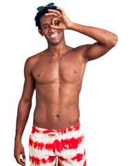 African handsome man wearing swimsuit and sunglasses doing ok gesture with hand smiling, eye looking through fingers with happy face.