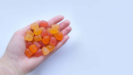 Group of red, orange and yellow multivitamin gummies in the hand isolated on white background