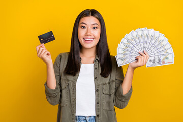 Photo of impressed ecstatic cheerful girl with brunette hair wear gray shirt hold debit card money isolated on yellow color background