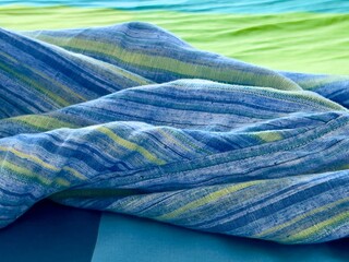 Detail view. Blue, green and indigo linen shirt dropped on a blue, green and indigo bed cover,...