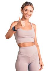 Beautiful caucasian woman wearing sportswear doing happy thumbs up gesture with hand. approving...