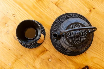 Schilderijen op glas Top view of a cast iron teapot and a tea cup, mug set on a wooden table © Damián Méndez/Wirestock Creators