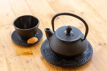 Tuinposter Top view of a cast iron teapot and a tea cup, mug set on a wooden table © Damián Méndez/Wirestock Creators
