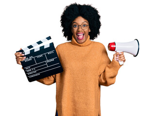 Young african american woman holding video film clapboard and megaphone celebrating crazy and...