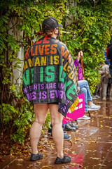 Fototapeta premium Woman standing at political rally on wet day wrapped in a love is Love All lives matter flag
