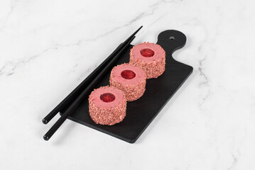 Vegan Red plum mousse cream cake, in the form of round sweet japanese sushi, on a serving board. White background.