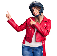 Young beautiful woman wearing motorcycle helmet smiling and looking at the camera pointing with two...