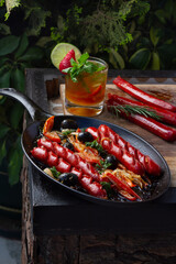 frying pan with sausages, black olives, rosemary. Outdoor with a beverage.
