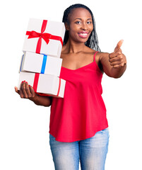 Young african american woman holding gift smiling happy and positive, thumb up doing excellent and approval sign