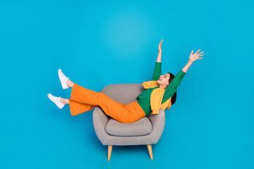 Full size profile portrait of overjoyed glad girl sit chair raise hands isolated on blue color background © deagreez