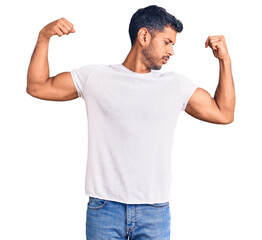 Young latin man wearing casual clothes showing arms muscles smiling proud. fitness concept.