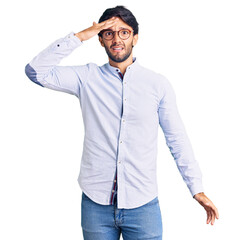 Handsome hispanic man wearing business shirt and glasses surprised with hand on head for mistake, remember error. forgot, bad memory concept.