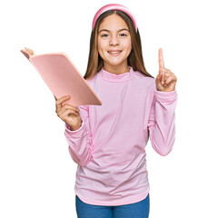 Beautiful brunette little girl reading a book surprised with an idea or question pointing finger with happy face, number one