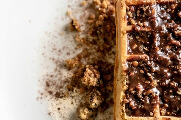 Closeup of a waffle with chocolate and cookie crumbs on a white plate in the kitchen
