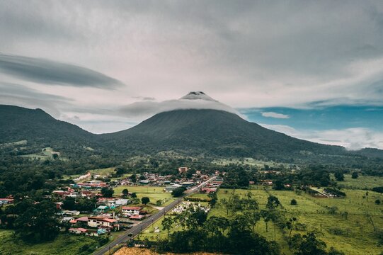 Scenic view of Arenal Volcano covered with clouds and a village at its base in Costa Rica