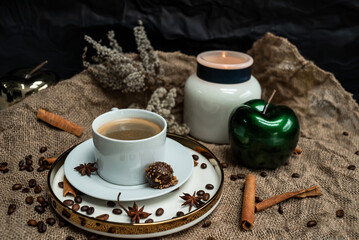 Background composition of a cup of coffee, candles, decorative apples, spices and dried flowers on a background of burlap
