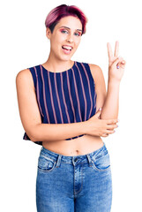 Young beautiful woman with pink hair wearing casual clothes smiling with happy face winking at the camera doing victory sign. number two.