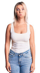 Young beautiful blonde woman wearing casual sleeveless t-shirt puffing cheeks with funny face. mouth inflated with air, crazy expression.