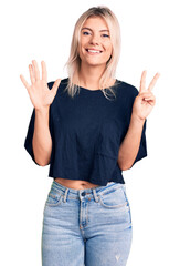 Young beautiful blonde woman wearing casual t-shirt showing and pointing up with fingers number seven while smiling confident and happy.