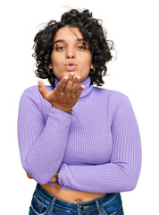 Fototapeta na wymiar Young hispanic woman with curly hair wearing casual clothes looking at the camera blowing a kiss with hand on air being lovely and sexy. love expression.