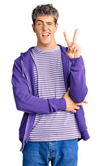 Young handsome man wearing casual purple sweatshirt smiling with happy face winking at the camera...
