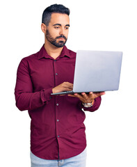 Young hispanic man holding laptop thinking attitude and sober expression looking self confident