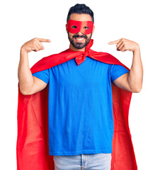 Young hispanic man wearing super hero costume looking confident with smile on face, pointing oneself with fingers proud and happy.