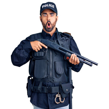 Young hispanic man wearing police uniform holding shotgun scared and amazed with open mouth for surprise, disbelief face