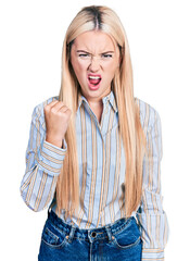 Beautiful blonde woman wearing casual striped shirt angry and mad raising fist frustrated and furious while shouting with anger. rage and aggressive concept.