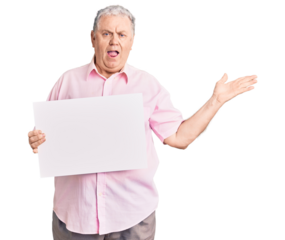 Senior grey-haired man holding blank empty banner celebrating victory with happy smile and winner expression with raised hands