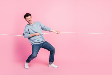 Full length photo of excited guy playing tug war game pull string isolated on pastel color...