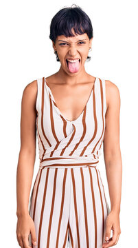 Young brunette woman with short hair wearing summer outfit sticking tongue out happy with funny expression. emotion concept.