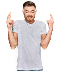 Fototapeta premium Young redhead man wearing casual grey t shirt gesturing finger crossed smiling with hope and eyes closed. luck and superstitious concept.