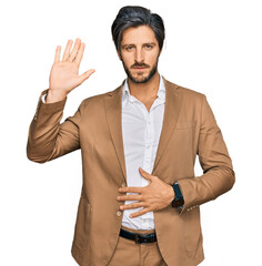 Young hispanic man wearing business clothes swearing with hand on chest and open palm, making a...