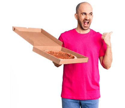 Young handsome man holding delivery pizza cardboard box pointing thumb up to the side smiling happy with open mouth