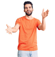 Naklejka premium Young handsome man with beard wearing casual t-shirt smiling cheerful offering hands giving assistance and acceptance.