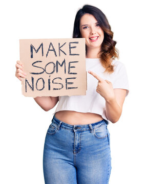 Beautiful young brunette woman holding make some noise banner smiling happy pointing with hand and finger