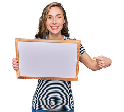 Young blonde woman holding empty white board smiling happy pointing with hand and finger