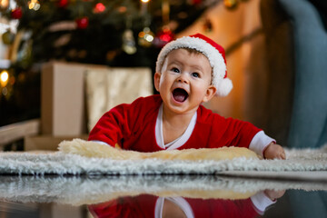 happy laughing baby in christmas outfit or santa claus dress crawling infront of xmas tree on a...