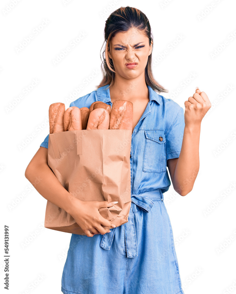 Sticker Young beautiful woman holding paper bag with bread annoyed and frustrated shouting with anger, yelling crazy with anger and hand raised