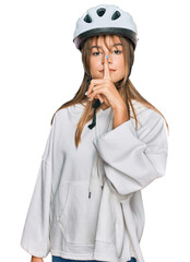 Teenager caucasian girl wearing bike helmet asking to be quiet with finger on lips. silence and...