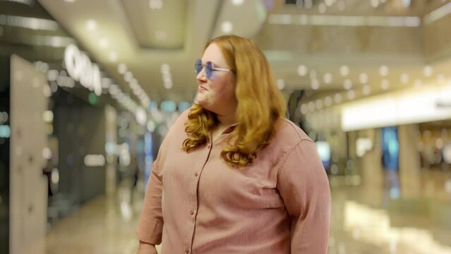 Young plus size woman taking off glasses and winking on cam in a shopping mall