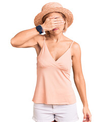 Young blonde woman wearing summer hat covering eyes with hand, looking serious and sad. sightless, hiding and rejection concept