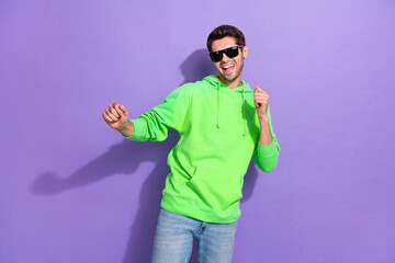 Fototapeta premium Photo of attractive positive handsome guy brunet hairdo dressed green hoodie dancing on party weekend isolated on purple color background