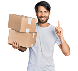 Hispanic man with blue eyes holding packages surprised with an idea or question pointing finger with happy face, number one